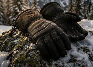 Pair of black leather ski gloves with tan suede accents and an adjustable buckle wrist strap on a white background.