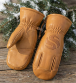 Tan leather winter mittens with reinforced palm grip and pine background