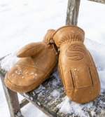 Tan leather winter mittens with reinforced palm grip and pine background