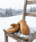 Tan leather winter mittens with reinforced palm grip and pine background