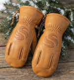 Tan leather winter mittens with reinforced palm grip and pine background