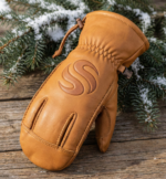 Tan leather winter mittens with reinforced palm grip and pine background